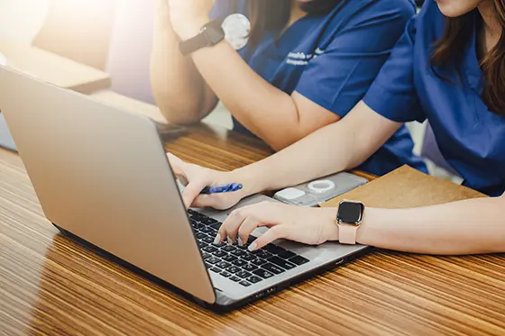 Two healthcare professionals using a laptop to prepare a medical certificate online.