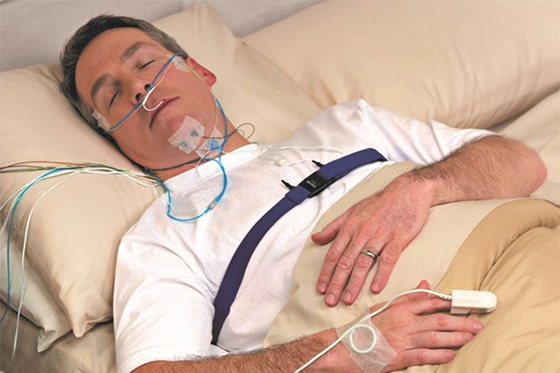 Man undergoing a sleep study with diagnostic equipment and sensors attached to his body.